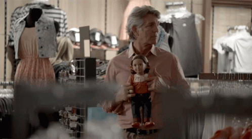 man holds his doll in the foreground while others are working on clothes