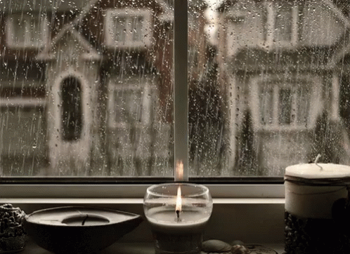 two candles sitting in a glass container by a window