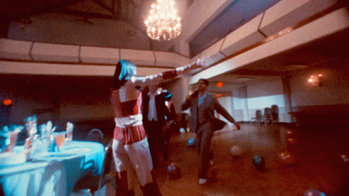a group of people dancing around a room with chandelier and tables
