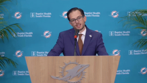 a man wearing glasses speaking from behind a podium
