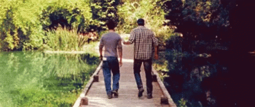 two people walking along a bridge toward a pond