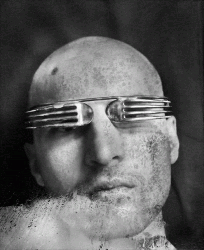 a bald headed man wearing metal frames and a mustache