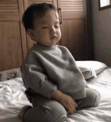 a baby in a white sweatshirt sits on the bed