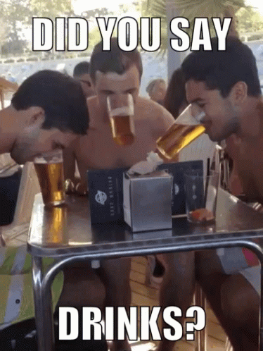 two men drink from cans at a table, while another man looks at them