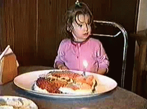 girl looking surprised by blue frosted cake with lit candles