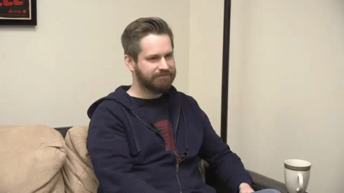man with beard sitting down on couch playing a video game