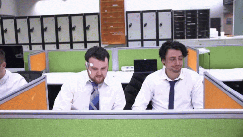 two men in ties sitting in cubicles at desks