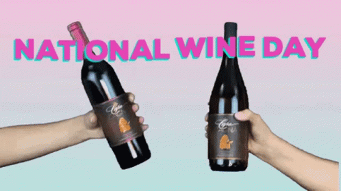 hands holding two bottles of wine with a national wine day sign in front of them