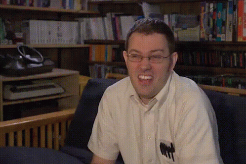 a young man with glasses laughing in front of a bookcase