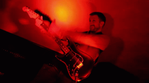 a man holding an electric guitar playing in the dark