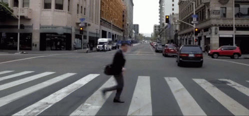 person walking across the crosswalk on the side of a busy city street