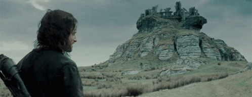 a man is on the edge of a hill, and there is an old structure that appears to be a castle