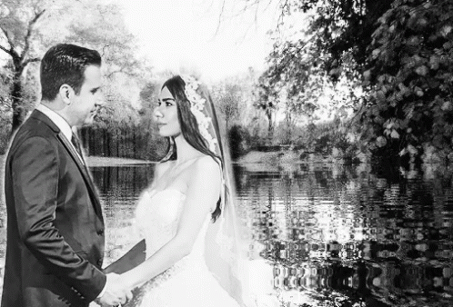 a bride and groom pose in front of water