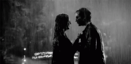 two people are standing in the rain in black and white