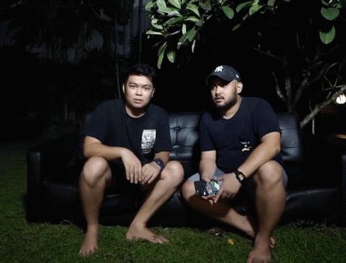 two asian men sitting on a sofa looking at soing
