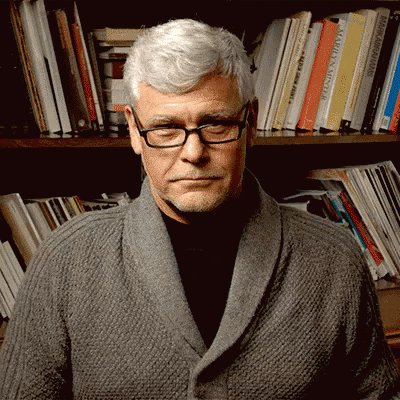 a man has white hair and glasses as he stands in front of a book shelf