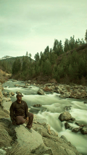 a person sitting on a rock near a river