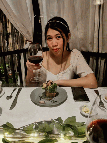 a woman that is sitting at a table with a glass of wine