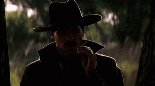 man wearing cowboy hat smoking cigarette in dark forest
