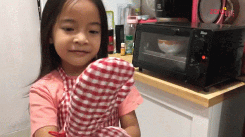 a little girl standing in front of a microwave oven holding a mitt