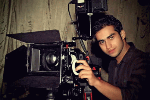 a young man poses for a picture behind a camera