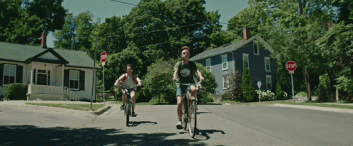 two bicyclists ride their bicycles through a suburban intersection