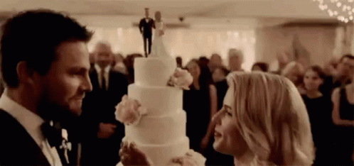 two people standing around a wedding cake in front of a crowd