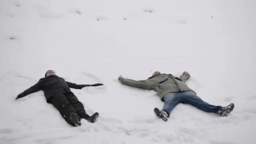 two men who are lying on some snow
