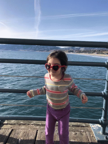 little girl standing on dock near water wearing sunglasses