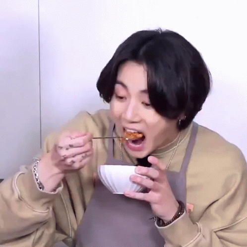 an asian woman taking a bite of a bowl of soup