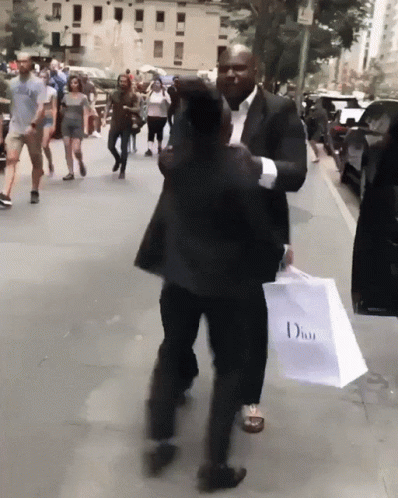 a man in a suit and tie carrying a pink bag and walking down the street