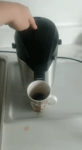 a hand with glove on holding coffee mug over top of coffee machine