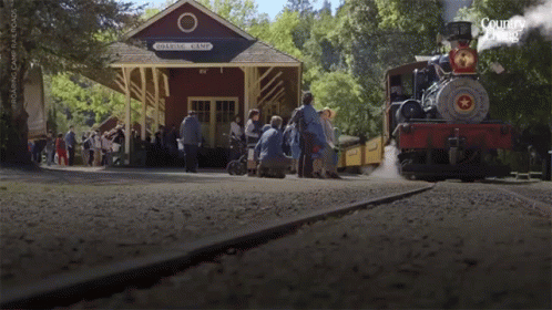 a train is pulling into a depot with people and smoke