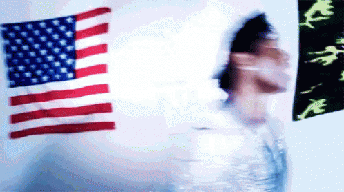 the blurry image shows the back of a woman in front of two american flags
