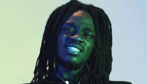 a man with long dreadlocks standing in front of a light green background
