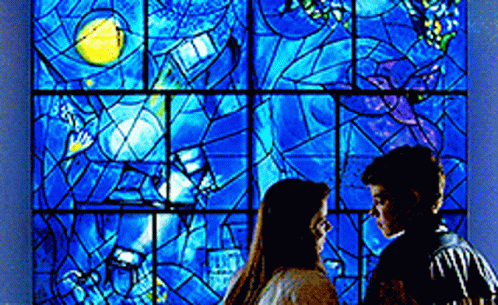 a couple is standing close to each other in front of a stained glass window