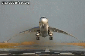 a silver airplane flying low to the ground with its landing gear down