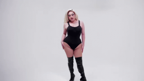 a woman wearing a bodysuit and boots poses