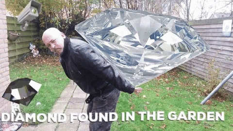 a man holding up an oversized diamond in a garden