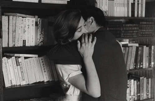 black and white pograph of two people kissing in front of bookshelves