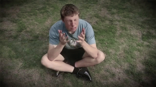a man sitting on the grass clapping and holding a soccer ball