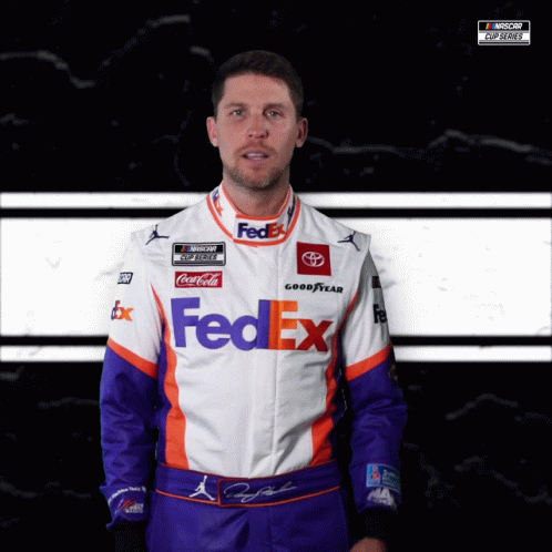 a man in a nascar uniform standing up for the camera