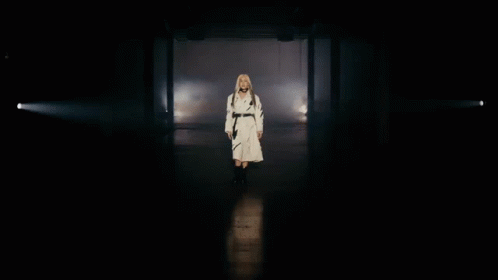 a woman in a robe walks through a darkened room