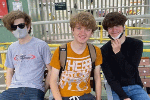 three male students are sitting on a bench and posing for a picture