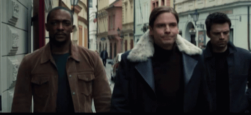 three men wearing coats walking down a street