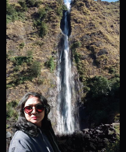 a man wearing sunglasses taking a selfie in front of a waterfall