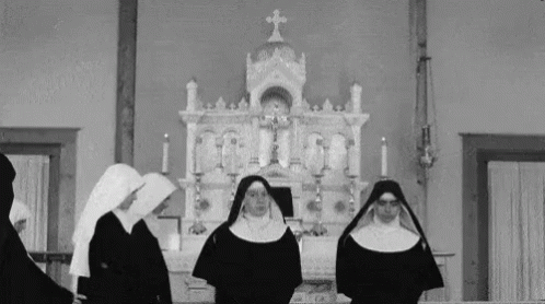 two nun women in black outfits and two of them wearing headscarves, while standing in front of the altar