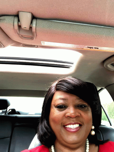 a woman in purple and pearls smiling in a car