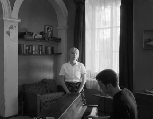black and white pograph of man playing the piano with a woman watching