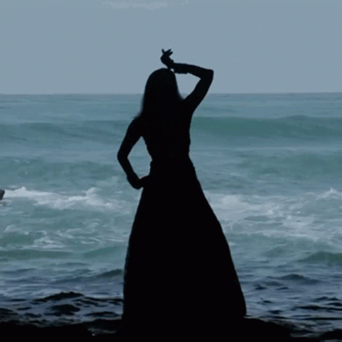 a girl in long dress standing on rocks near the ocean